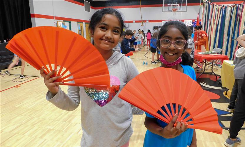 Two girls smile while holding red fans